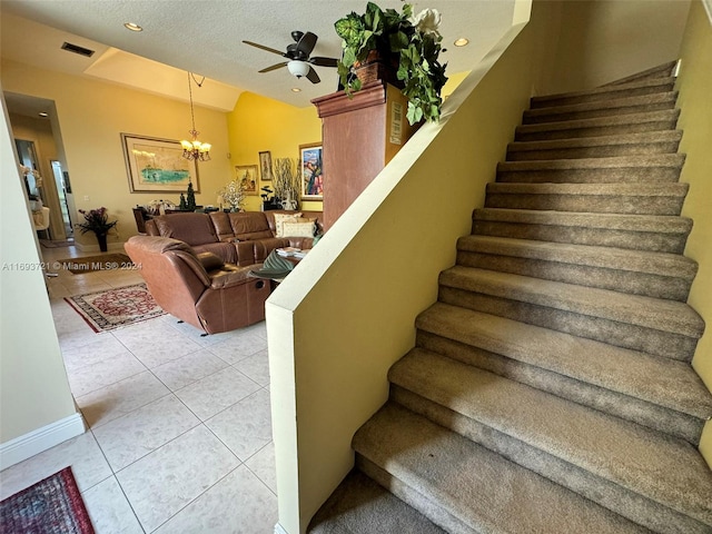 staircase with tile patterned flooring, a textured ceiling, and ceiling fan with notable chandelier