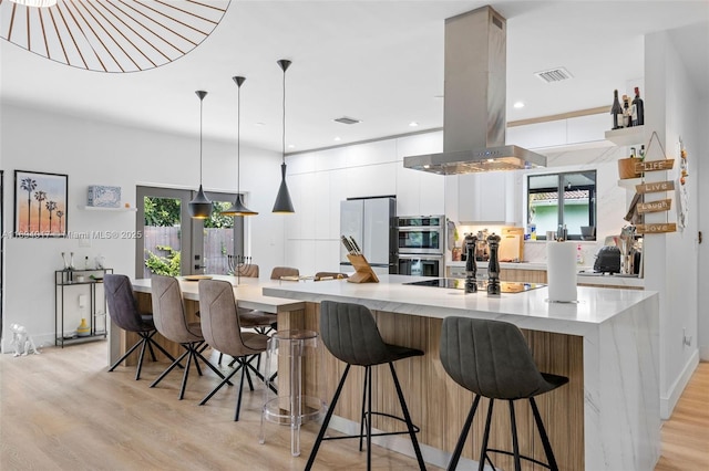 kitchen with white cabinetry, decorative light fixtures, white refrigerator, island exhaust hood, and stainless steel double oven