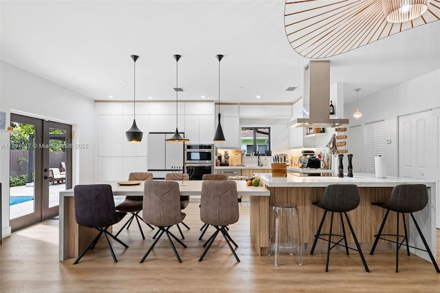 kitchen with french doors, island range hood, decorative light fixtures, and a breakfast bar