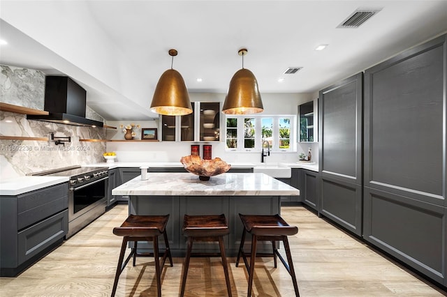 kitchen featuring a kitchen breakfast bar, stainless steel range with electric stovetop, wall chimney exhaust hood, decorative light fixtures, and light hardwood / wood-style floors