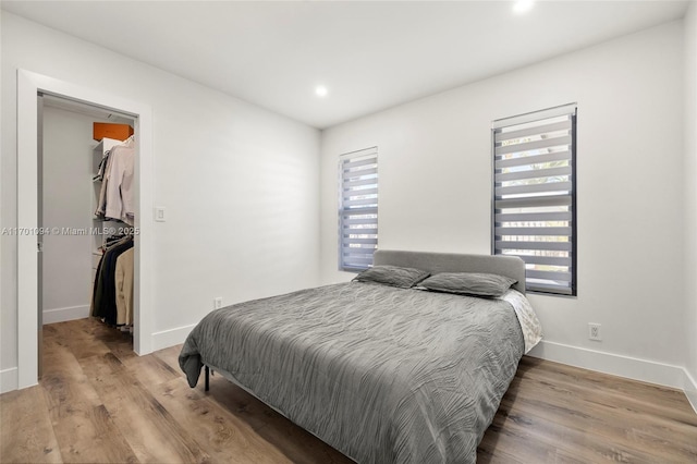 bedroom with wood finished floors, a walk in closet, and baseboards