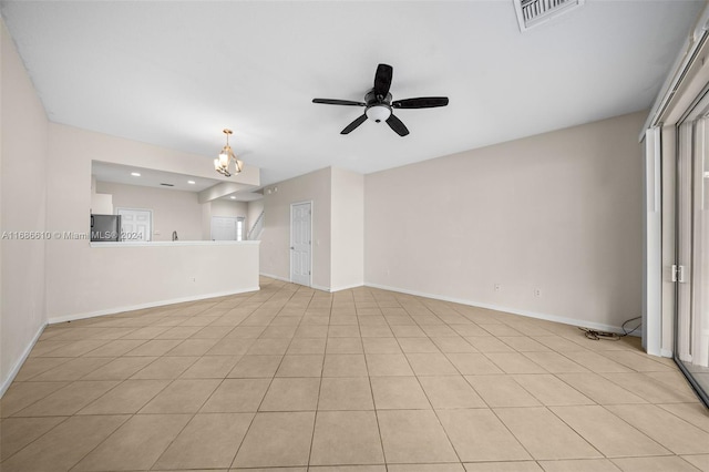 tiled spare room featuring ceiling fan with notable chandelier