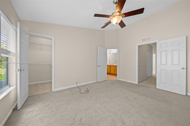 unfurnished bedroom featuring a walk in closet, ceiling fan, connected bathroom, light colored carpet, and a closet