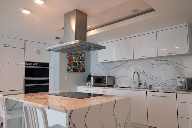 kitchen featuring tasteful backsplash, island exhaust hood, white cabinetry, and light stone countertops