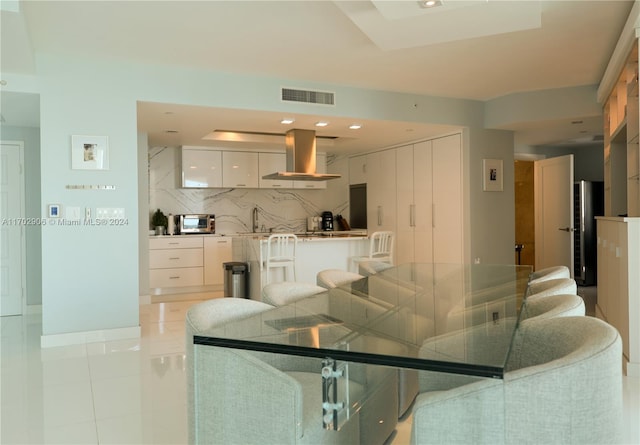 kitchen featuring white cabinets, range hood, backsplash, a breakfast bar area, and light tile patterned floors