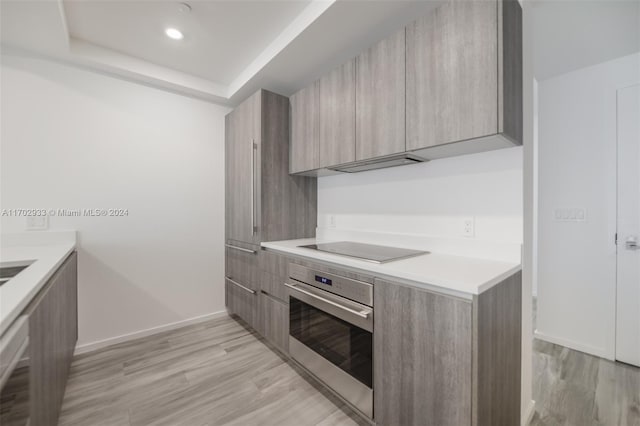 kitchen with black electric cooktop, light hardwood / wood-style flooring, a tray ceiling, and stainless steel oven