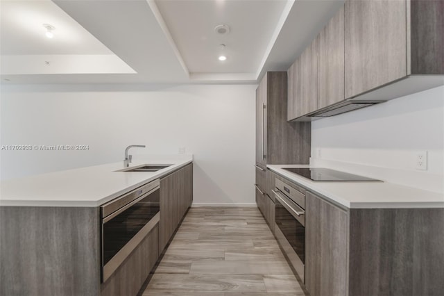 kitchen with black electric cooktop, a raised ceiling, sink, light hardwood / wood-style floors, and oven