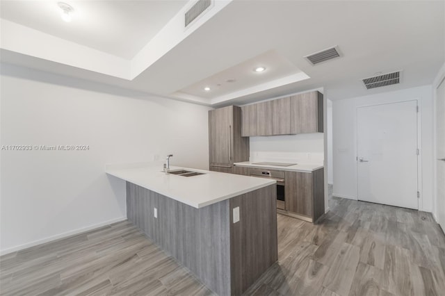 kitchen with sink, kitchen peninsula, light hardwood / wood-style floors, a tray ceiling, and black electric cooktop