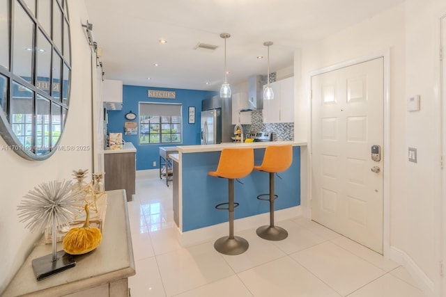 kitchen with pendant lighting, tasteful backsplash, light tile patterned flooring, a kitchen bar, and white cabinetry