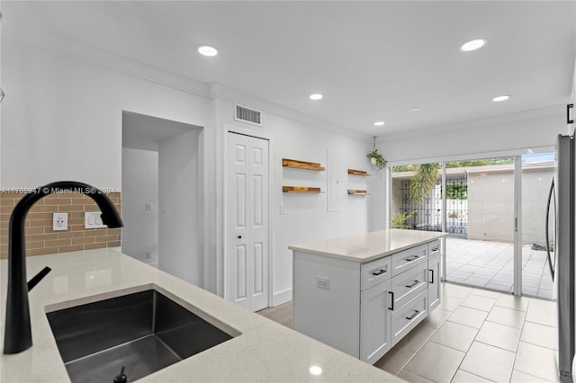 kitchen with white cabinets, ornamental molding, sink, and stainless steel refrigerator