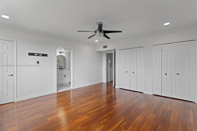 unfurnished bedroom featuring ensuite bathroom, crown molding, ceiling fan, dark hardwood / wood-style flooring, and multiple closets