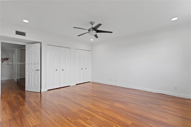 unfurnished bedroom featuring multiple closets, ceiling fan, dark hardwood / wood-style flooring, and ornamental molding