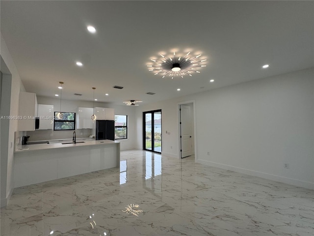 kitchen with hanging light fixtures, black refrigerator, sink, and white cabinets