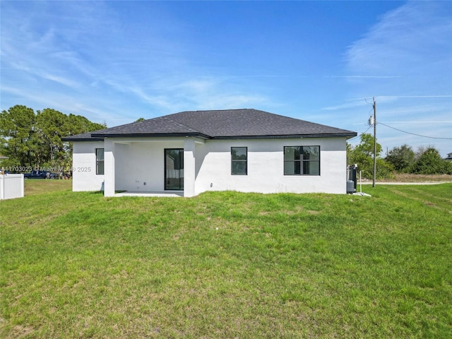 rear view of property with roof with shingles, a lawn, and stucco siding