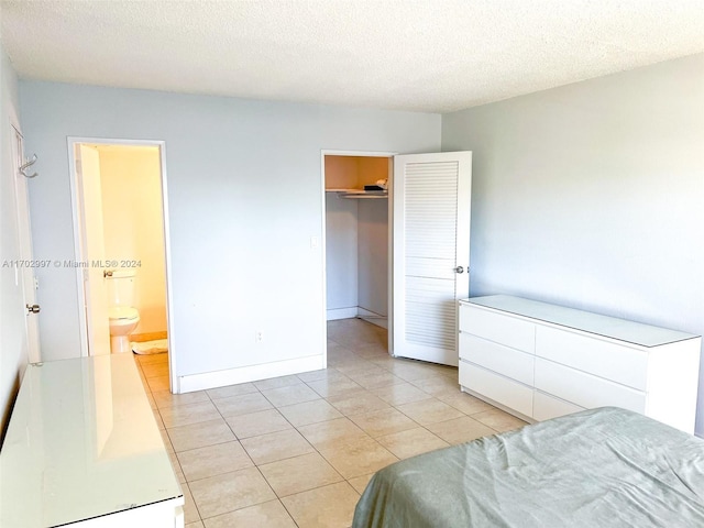 bedroom with a walk in closet, ensuite bathroom, a textured ceiling, light tile patterned floors, and a closet