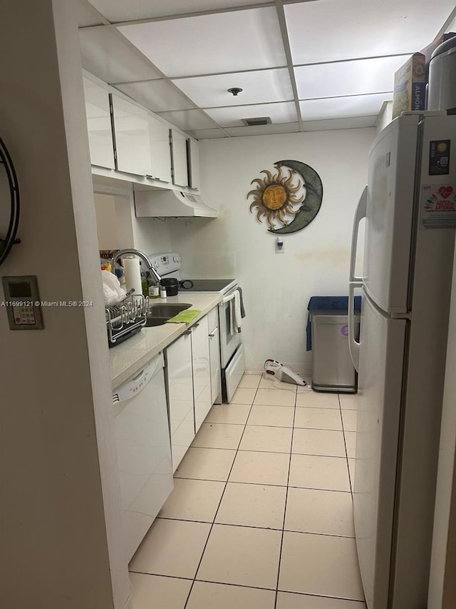 kitchen featuring a drop ceiling, white cabinets, light tile patterned flooring, and white appliances