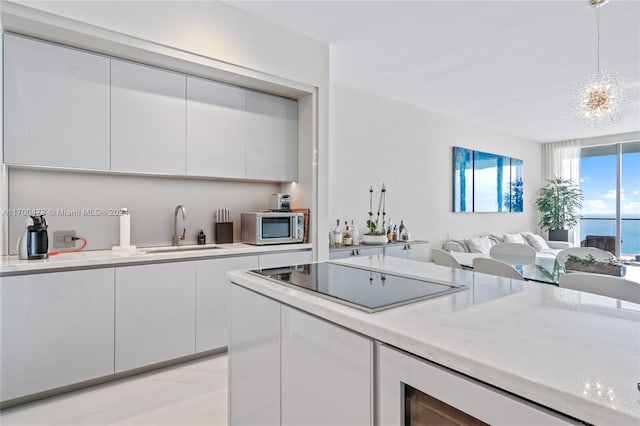 kitchen with black electric cooktop, sink, decorative light fixtures, a water view, and white cabinets