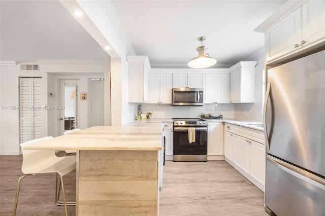 kitchen featuring hanging light fixtures, appliances with stainless steel finishes, crown molding, white cabinets, and light wood-type flooring