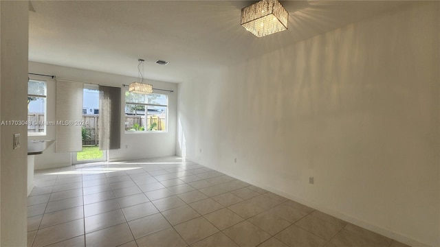 spare room featuring light tile patterned floors and a notable chandelier