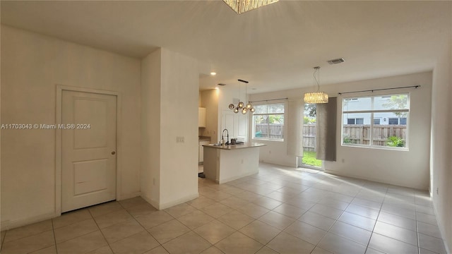 kitchen featuring white cabinetry, a notable chandelier, an island with sink, decorative light fixtures, and light tile patterned flooring