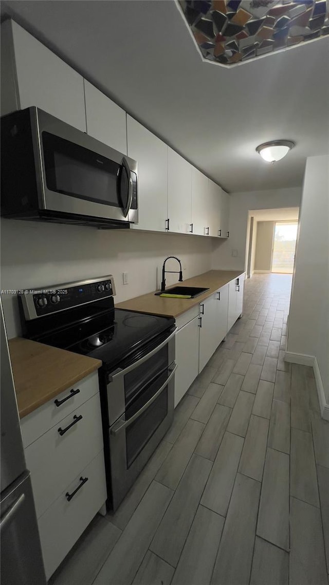 kitchen with appliances with stainless steel finishes, white cabinetry, and sink