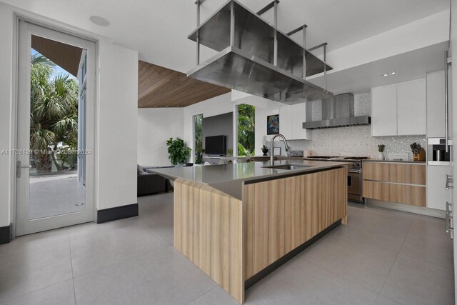 kitchen featuring high end range, tasteful backsplash, sink, wall chimney range hood, and white cabinetry