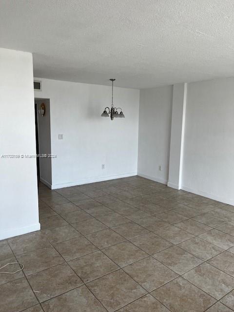 tiled empty room featuring a textured ceiling and an inviting chandelier