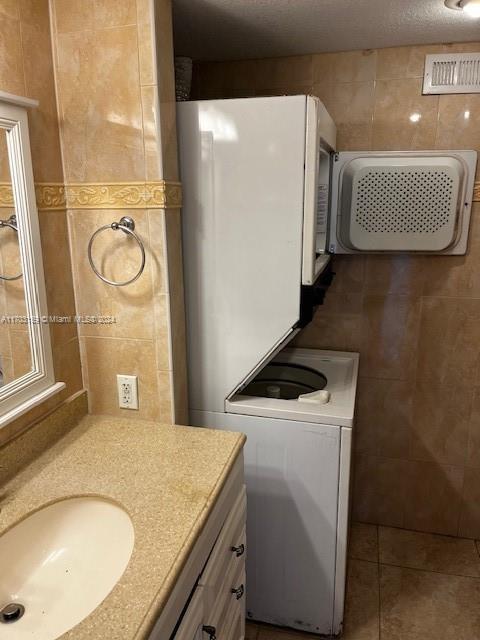 clothes washing area with sink, dark tile patterned floors, and tile walls