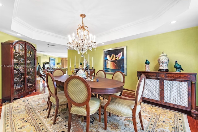 dining area featuring wood-type flooring, a tray ceiling, an inviting chandelier, and crown molding