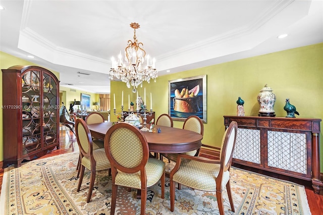 dining area with ornamental molding, a raised ceiling, a notable chandelier, and wood finished floors