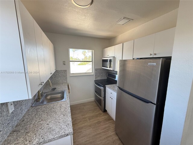 kitchen featuring sink, a textured ceiling, appliances with stainless steel finishes, light hardwood / wood-style floors, and white cabinetry