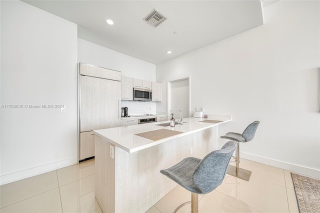 kitchen with a kitchen bar, appliances with stainless steel finishes, kitchen peninsula, sink, and light tile patterned flooring