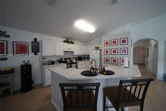 kitchen with lofted ceiling, white refrigerator, electric range, a kitchen bar, and white cabinetry