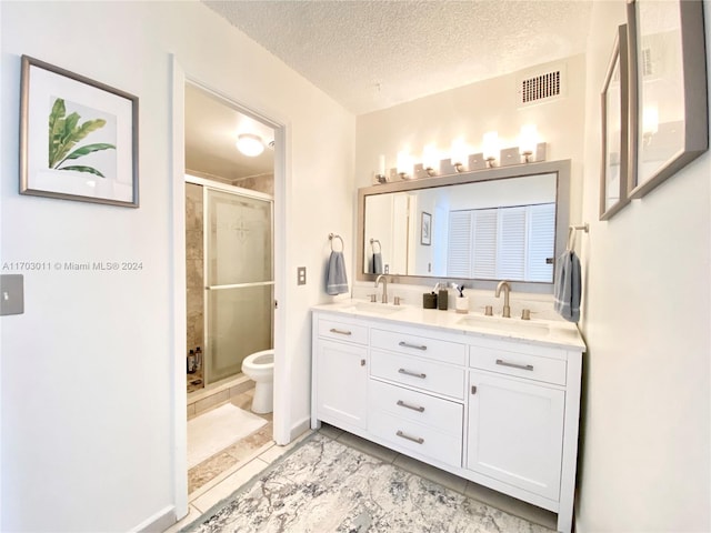 bathroom featuring vanity, a textured ceiling, a shower with door, tile patterned flooring, and toilet