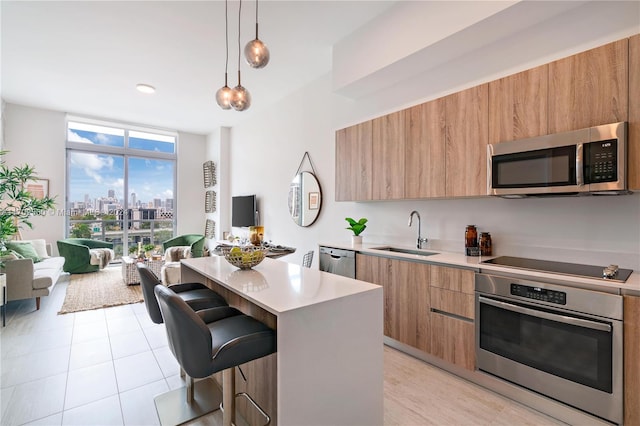 kitchen with sink, stainless steel appliances, decorative light fixtures, a breakfast bar area, and a kitchen island