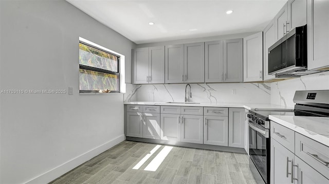 kitchen featuring gray cabinets, decorative backsplash, light wood-style floors, stainless steel range with electric cooktop, and a sink