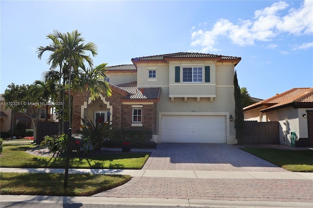 mediterranean / spanish house featuring a tiled roof, fence, a garage, stucco siding, and decorative driveway