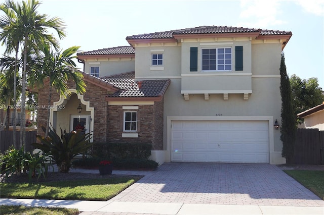 mediterranean / spanish-style home featuring decorative driveway, stucco siding, fence, stone siding, and a tiled roof