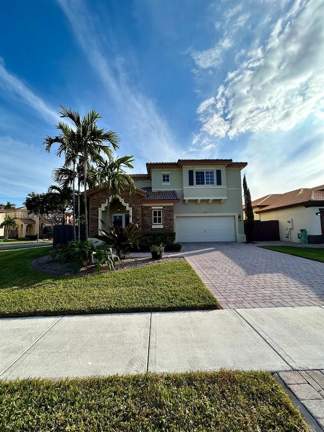 traditional home featuring stone siding, a garage, a front yard, stucco siding, and decorative driveway