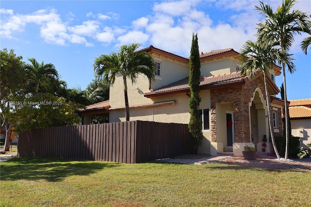 view of side of home with a tile roof, stucco siding, a lawn, fence, and stone siding