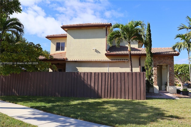 view of property exterior featuring fence, a yard, stone siding, a tiled roof, and stucco siding