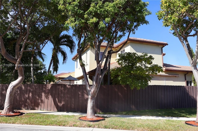 view of side of home featuring a tiled roof, fence, and stucco siding