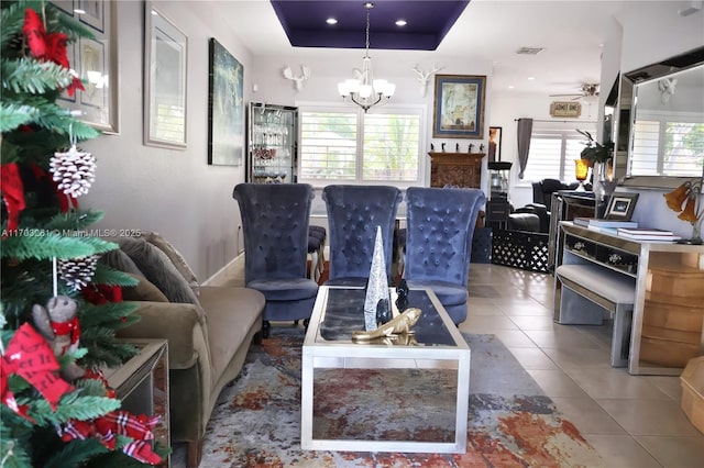 living area with tile patterned flooring, recessed lighting, ceiling fan with notable chandelier, visible vents, and a tray ceiling