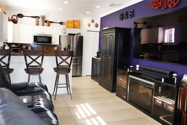 kitchen with tasteful backsplash, dark countertops, a breakfast bar, stainless steel appliances, and white cabinets