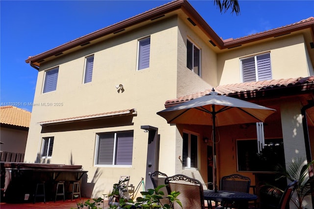 back of house featuring a hot tub, a tiled roof, a patio, and stucco siding