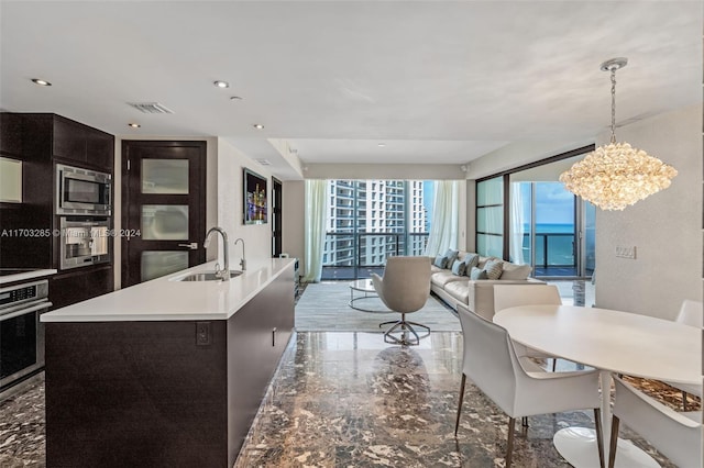 kitchen featuring appliances with stainless steel finishes, sink, pendant lighting, a center island with sink, and a notable chandelier