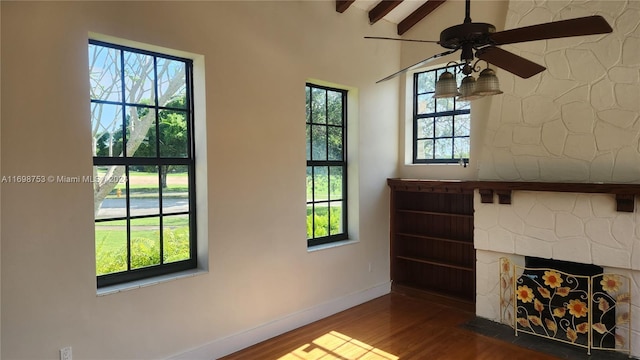 unfurnished living room featuring beam ceiling, dark hardwood / wood-style flooring, a wealth of natural light, and ceiling fan