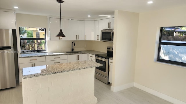 kitchen featuring sink, a healthy amount of sunlight, stainless steel appliances, decorative light fixtures, and a kitchen island