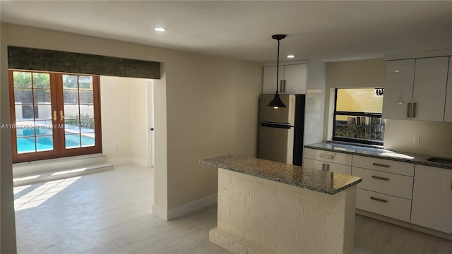 kitchen with french doors, light wood-type flooring, dark stone countertops, a center island, and stainless steel refrigerator