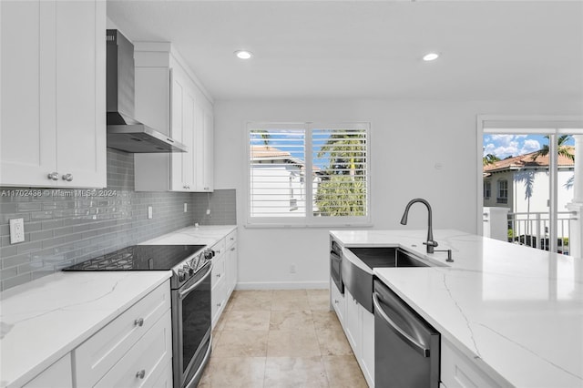 kitchen with light stone countertops, stainless steel appliances, white cabinets, and wall chimney exhaust hood